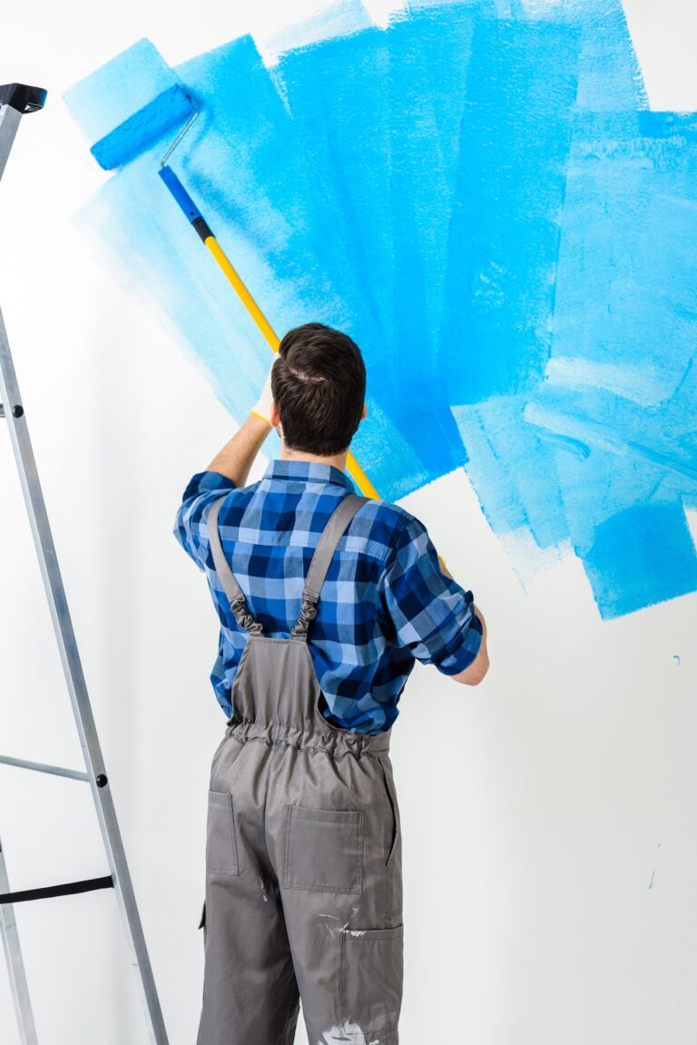 rear view of man painting wall with blue paint